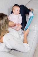 Mother showing story book to her baby in living room