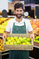 Smiling male staff holding a basket of green apple at supermarket