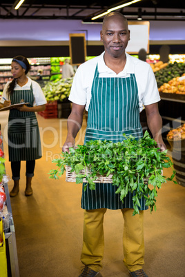 Smiling male staff holding a basket of fresh vegetables at supermarket