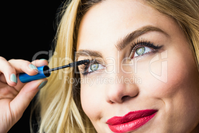 Beautiful woman applying mascara on eyelashes against black background
