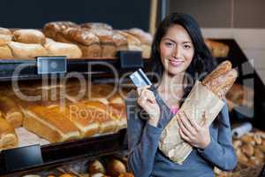 Woman holding baguettes and credit card at bread counter