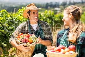Happy farmer couple holding baskets of vegetables and fruits