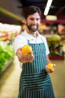 Smiling male staff showing fruit in organic section of supermarket