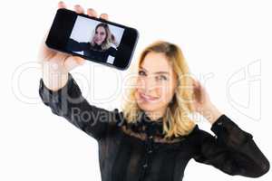 Smiling woman clicking photo from mobile phone against white background