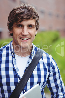 Smiling student standing in campus with digital tablet