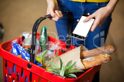 Woman holding groceries and mobile phone in supermarket