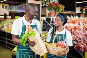 Smiling staffs holding basket and paper bag of vegetables