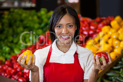 Smiling female staff holding bell peppers in organic section