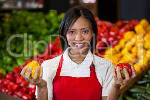 Smiling female staff holding bell peppers in organic section