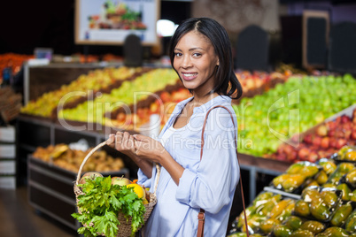 Smiling woman holding fruits and vegetables in basket