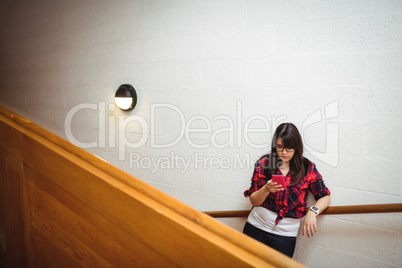 Female student standing on staircase and using mobile phone