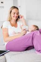 Mother talking on mobile phone while feeding her baby with milk bottle