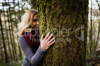 Beautiful woman hiding behind tree trunk in forest