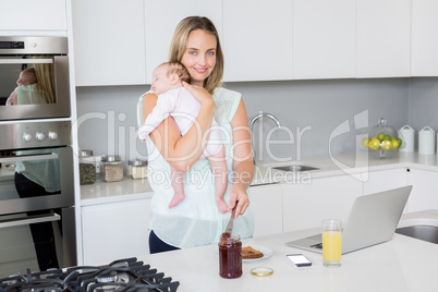 Portrait of mother putting jam on bread while carrying her baby