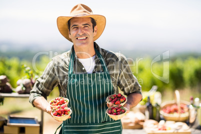 Portrait of a smiling farmer holding bowls of strawberries