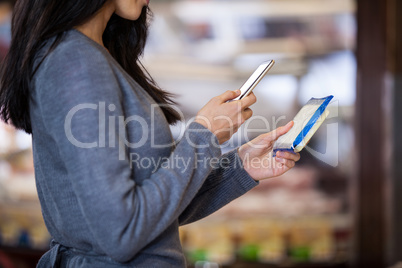 Woman holding dairy product and using mobile phone