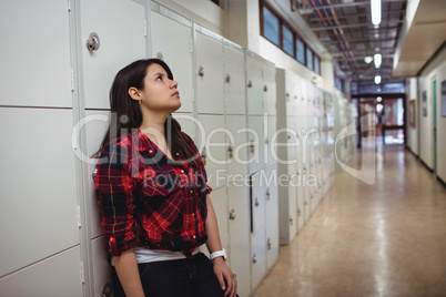 Sad female student leaning on locker