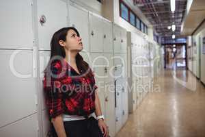 Sad female student leaning on locker