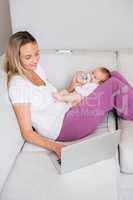 Mother using laptop while feeding her baby with milk bottle
