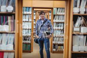 Student standing in library with laptop and digital tablet