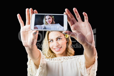 Smiling woman clicking photo from mobile phone against black background