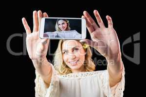 Smiling woman clicking photo from mobile phone against black background
