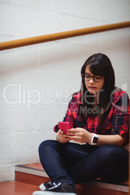 Female student sitting on staircase and using mobile phone