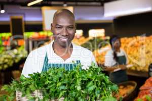 Smiling male staff holding a basket of fresh vegetables at supermarket