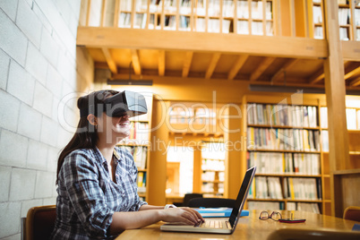 Female student using laptop and virtual reality headset in library