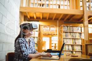 Female student using laptop and virtual reality headset in library
