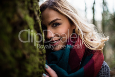 Beautiful woman hiding behind tree trunk in forest