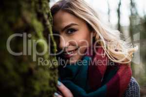 Beautiful woman hiding behind tree trunk in forest