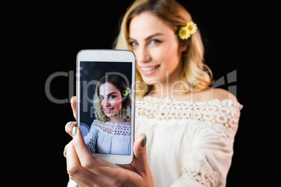 Beautiful woman clicking photo from mobile phone against black background