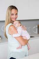 Mother carrying her baby in kitchen at home