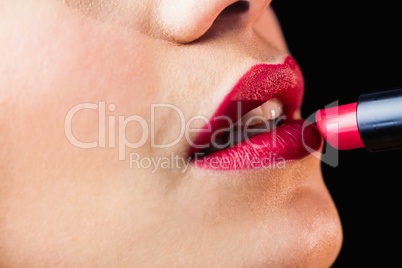 Beautiful woman applying red lipstick on lips against black background