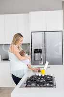 Mother using laptop while carrying baby in kitchen