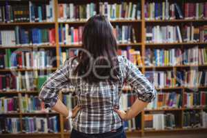Rear view of female student looking at books in the shelf