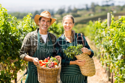 Portrait of happy farmer couple holding baskets of vegetables