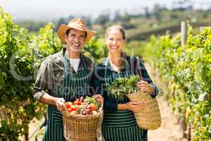 Portrait of happy farmer couple holding baskets of vegetables
