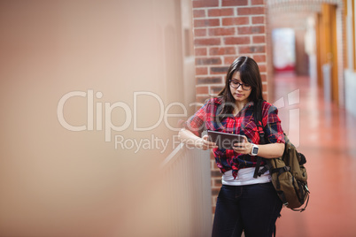 Female student using digital tablet in corridor