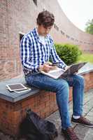 Student sitting with laptop using mobile phone in campus