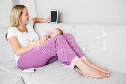 Mother using digital tablet while feeding her baby with milk bottle