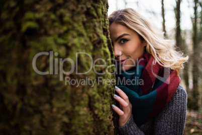 Beautiful woman hiding behind tree trunk in forest