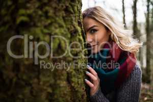 Beautiful woman hiding behind tree trunk in forest