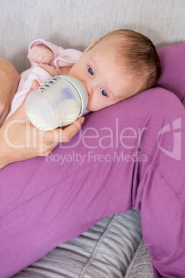 Mother feeding baby with milk bottle in living room