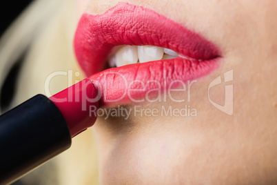 Beautiful woman applying red lipstick on lips against black background
