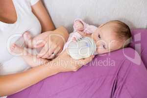 Mother feeding baby with milk bottle in living room