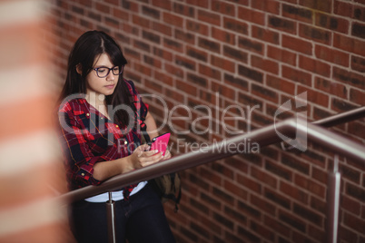 Female student walking on staircase while using mobile phone