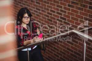 Female student walking on staircase while using mobile phone