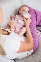 Mother feeding baby with milk bottle in living room
